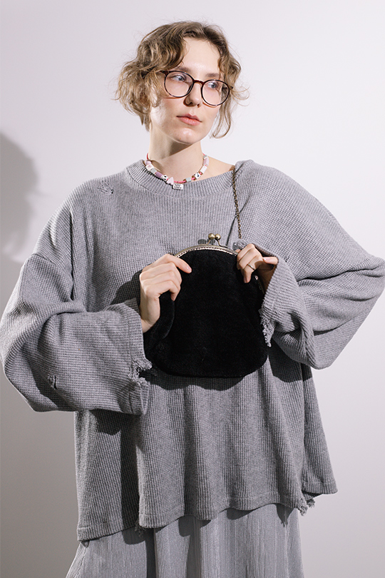 Портрет девушки с короткой стрижкой в сером свитере и черной сумкой в руке.